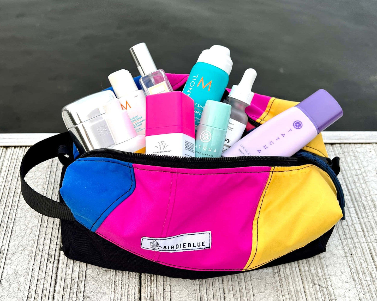 A lifestyle photo of the BirdieBlue Traveler on the dock filled with cosmetics and toiletries