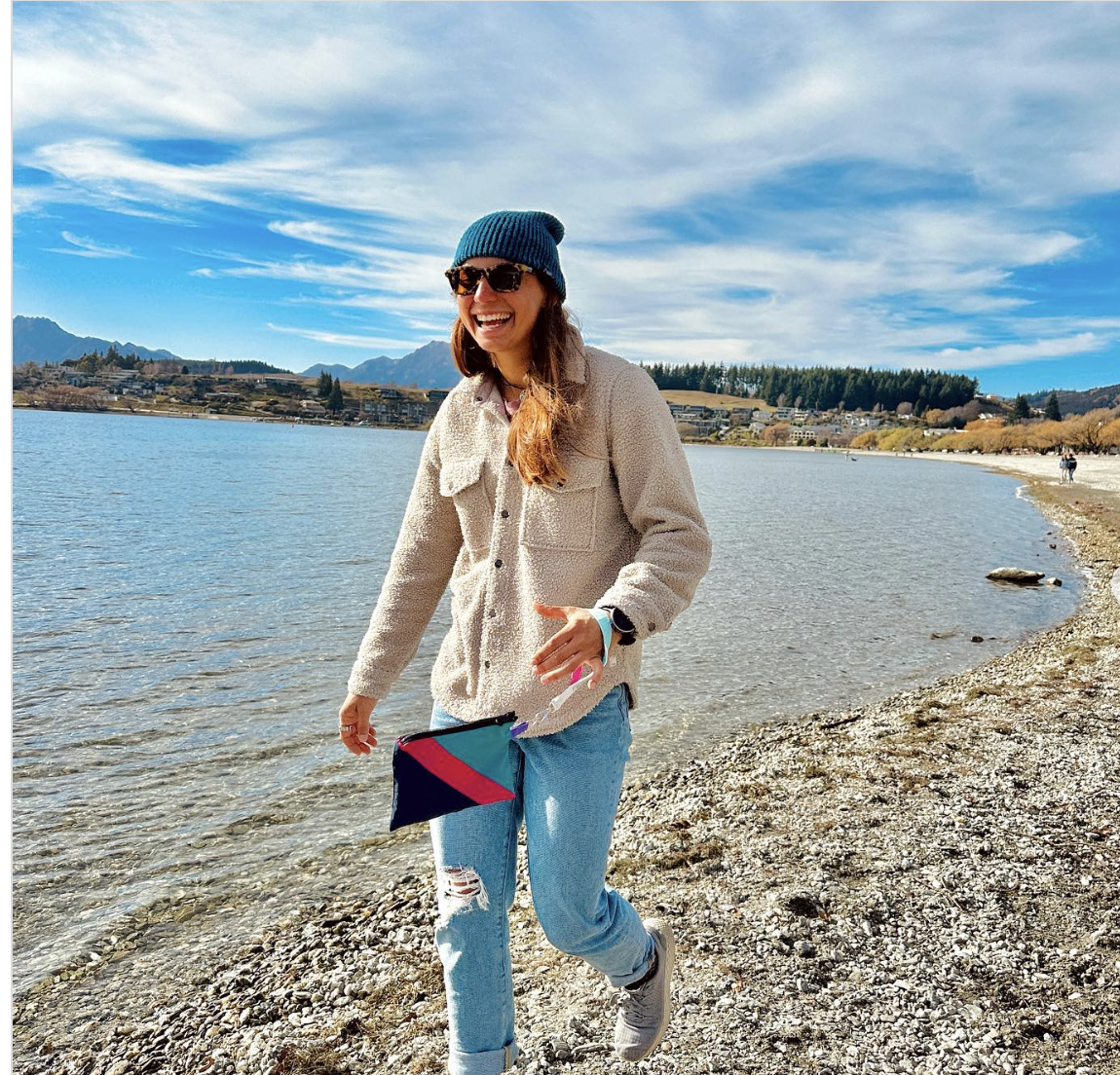 woman smiling walking on beach with colorful wristlet bag