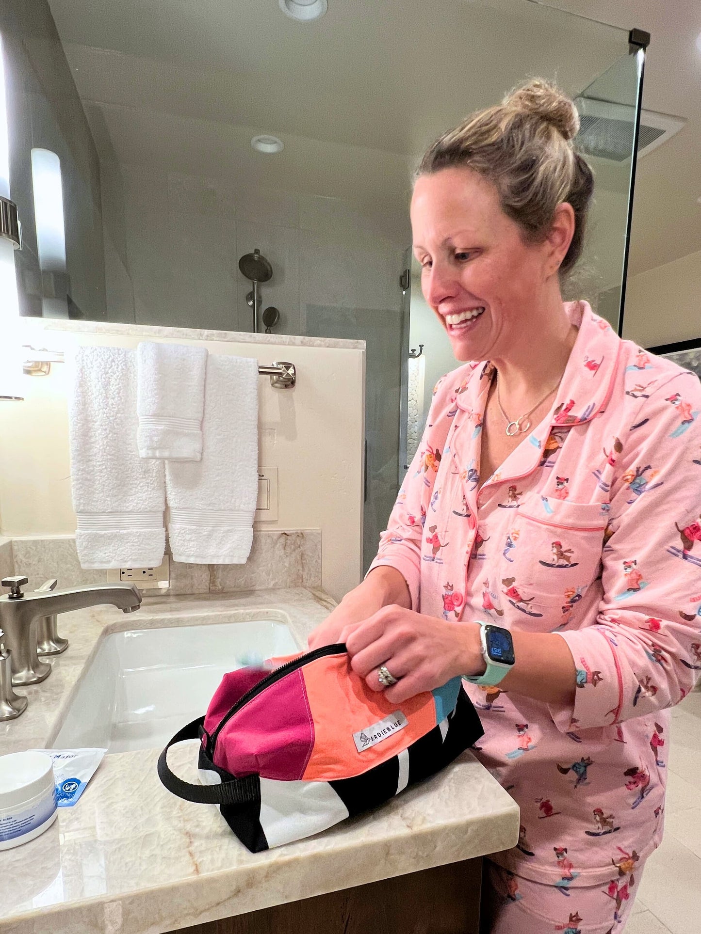 A lifestyle photo of person standing at a bathroom sink, organizing a small orange and black toiletry traveler bag.
