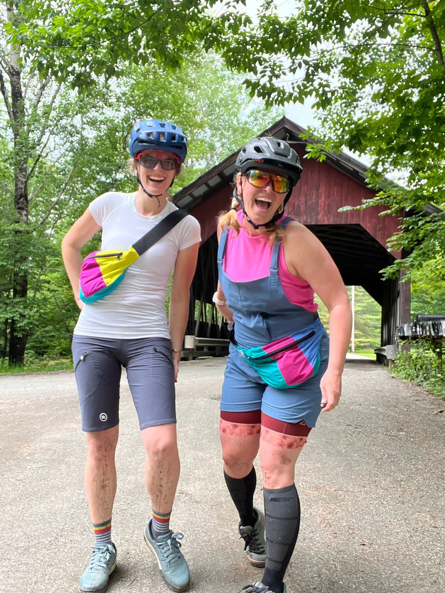 Two women laughing in mountain biking clothes and wearing two colorful recycled fanny packs