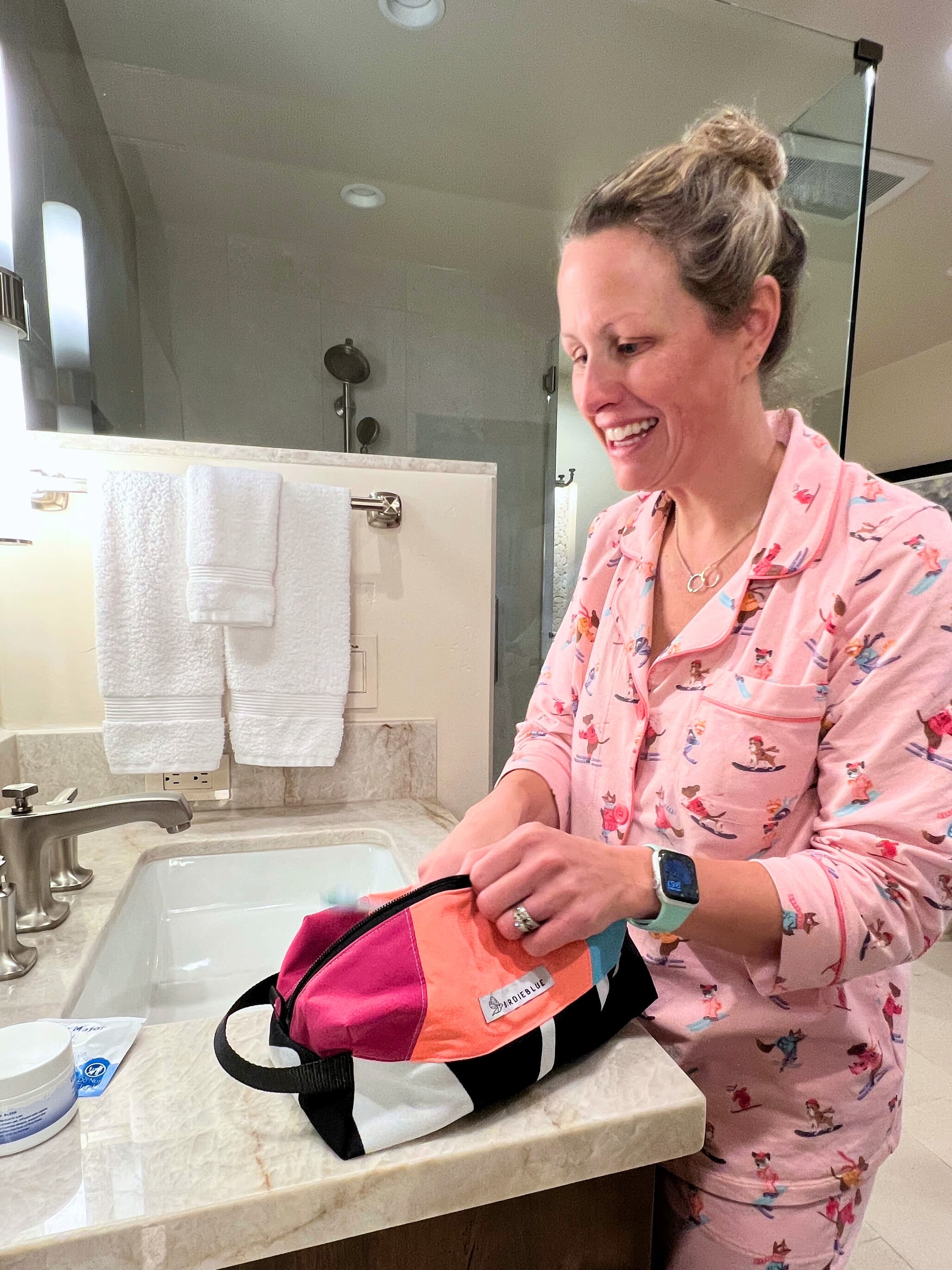 A lifestyle photo of person standing at a bathroom sink, organizing a small orange and black toiletry traveler bag.