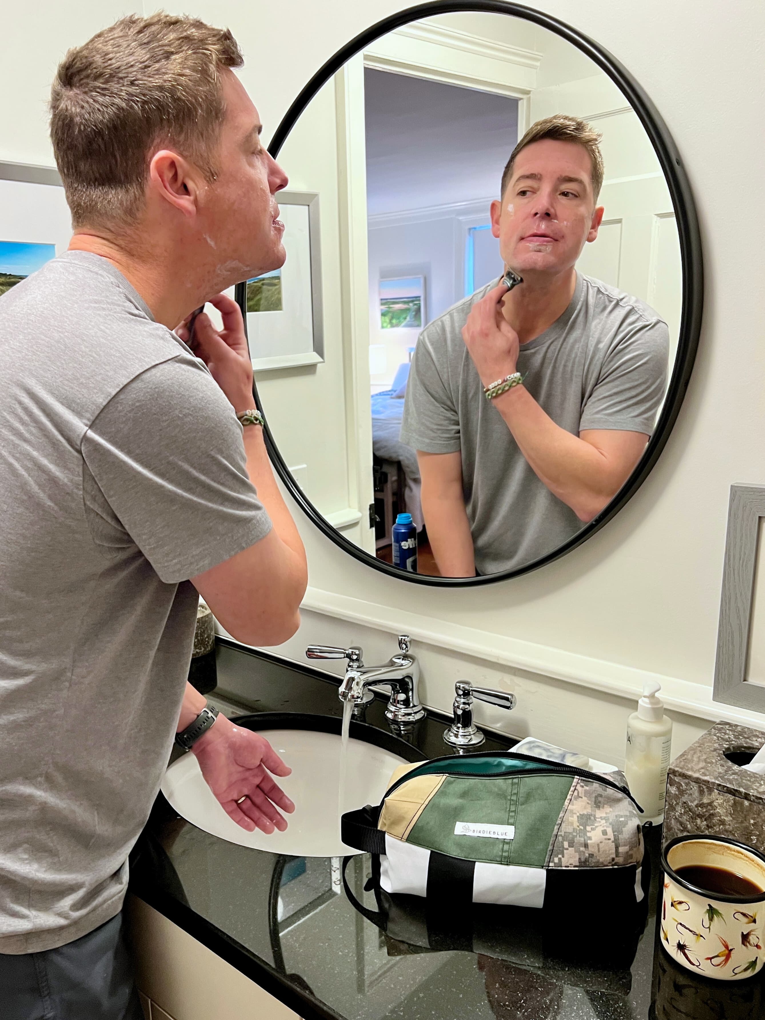 A lifestyle photo of person standing at a bathroom sink, shaving with their travel toiletry bag.