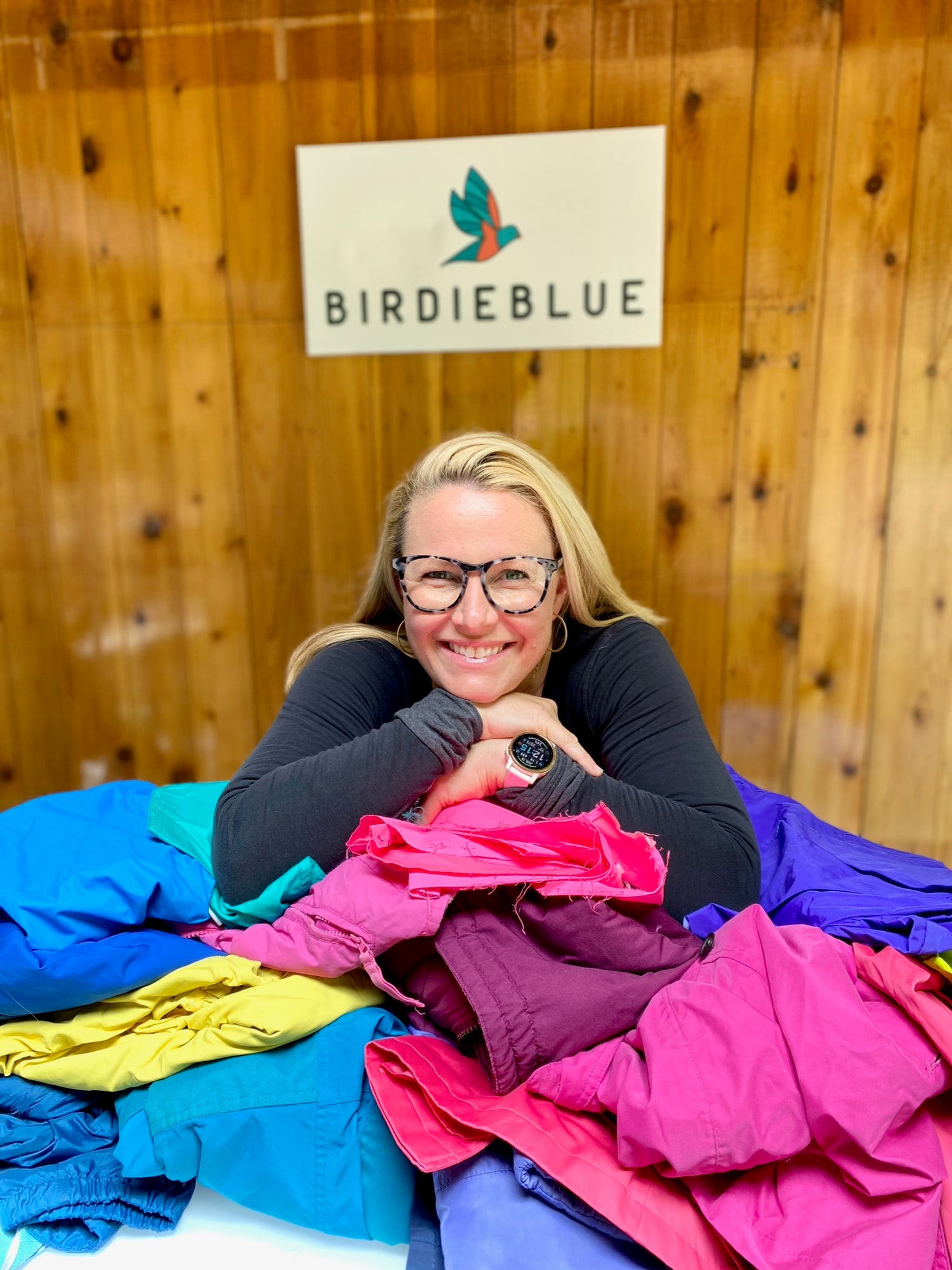 Woman smiling with piles of old ski and snowboard clothing