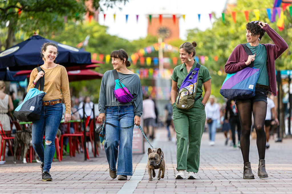 Women walking in a city with a french bulldog laughing and carrying bright colored tote bags