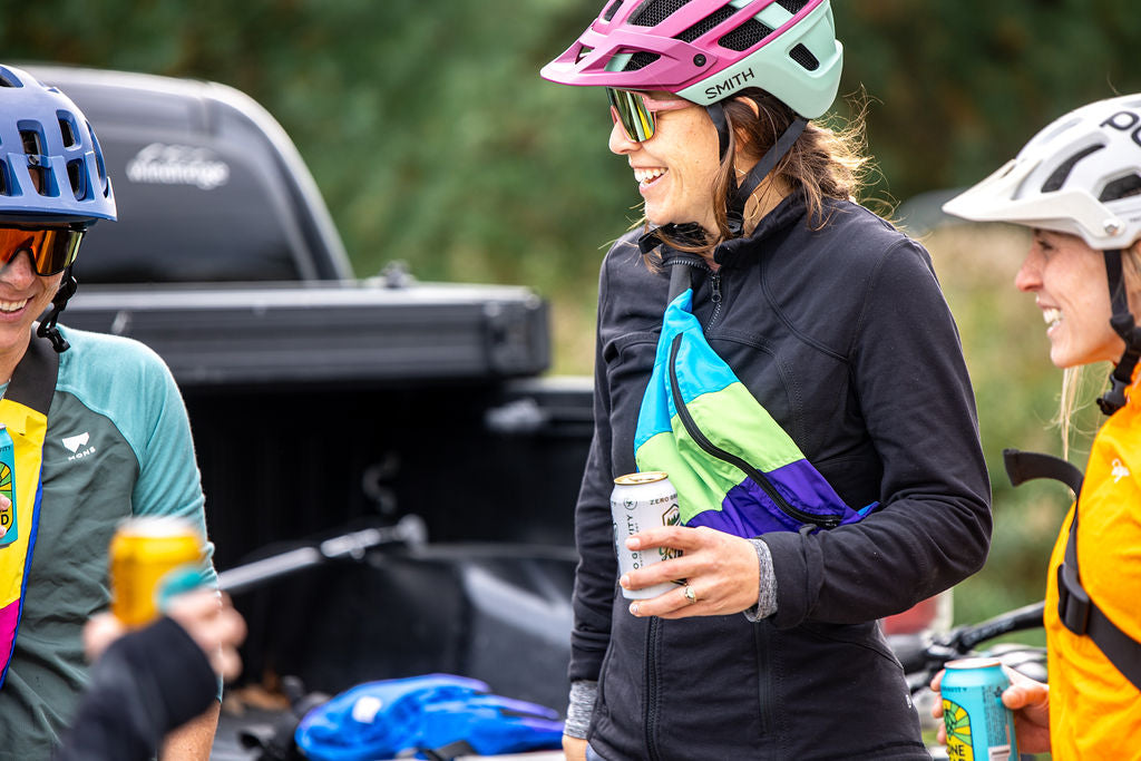 Woman smiling mountain biking with a colorful fanny drinking a beer